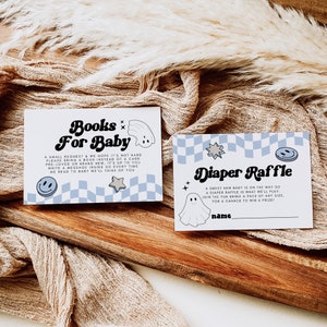 May include: Two baby shower cards on a wooden surface. One card reads "Books For Baby" with a ghost and smiley face graphic. The other card reads "Diaper Raffle" with a ghost and star graphic. Both cards have a blue and white checkered pattern.