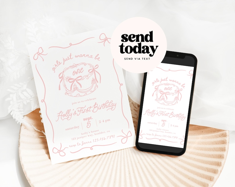 May include: A white invitation and a smartphone displaying a first birthday party invitation. The invitation features pink text and a cake graphic with the words "girls just wanna be one." The phone is black with a white background.