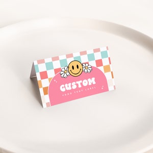 May include: Pink and orange food tent label with a checkered background. The label features a smiling face with flowers and the text "CUSTOM FOOD TENT LABEL".