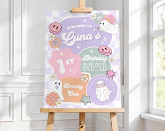 May include: A decorative sign on a wooden easel. The sign features a pastel color scheme with the words "Welcome to Luna's 1st Birthday Bash" and other text. The design includes smiley faces, ghosts, flowers, and stars.