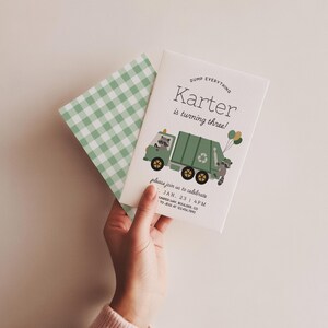 May include: A birthday invitation with a green garbage truck illustration, raccoons, and balloons. The text reads "Karter is turning three!" with event details. A green and white gingham envelope is also visible.