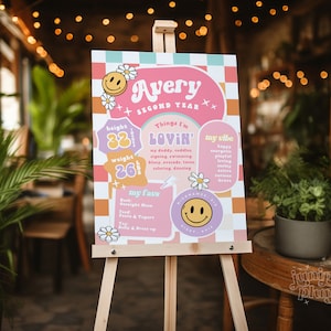 May include: A pink and purple birthday sign with the name Avery and the text "Second Year". The sign also includes details about Avery's height, weight, and favorite things. The sign is decorated with daisies and smiley faces.