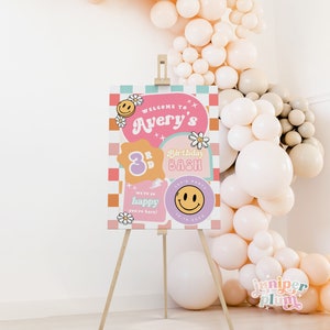 May include: A pink and orange welcome sign with a checkered background. The sign says "Welcome to Avery's 3rd Birthday Bash". There are smiley faces, flowers, and lightning bolts on the sign.