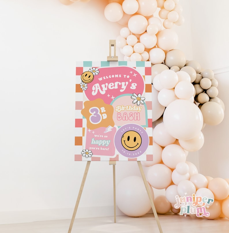 May include: A pink and orange welcome sign with a checkered background. The sign says "Welcome to Avery's 3rd Birthday Bash". There are smiley faces, flowers, and lightning bolts on the sign.