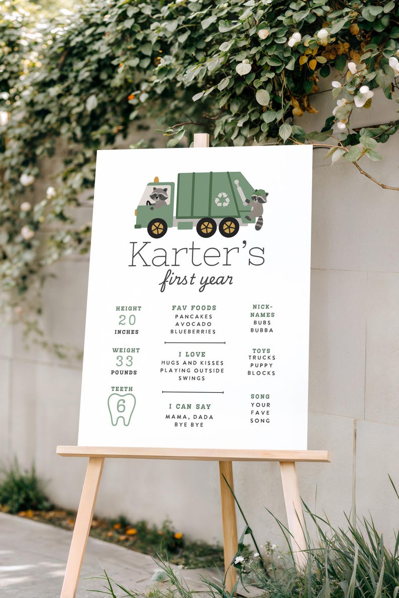 May include: A white sign on a wooden easel with the text "Karter's first year." The sign features a green garbage truck with raccoons. It lists height as 51 cm, weight as 15 kg, and 6 teeth.