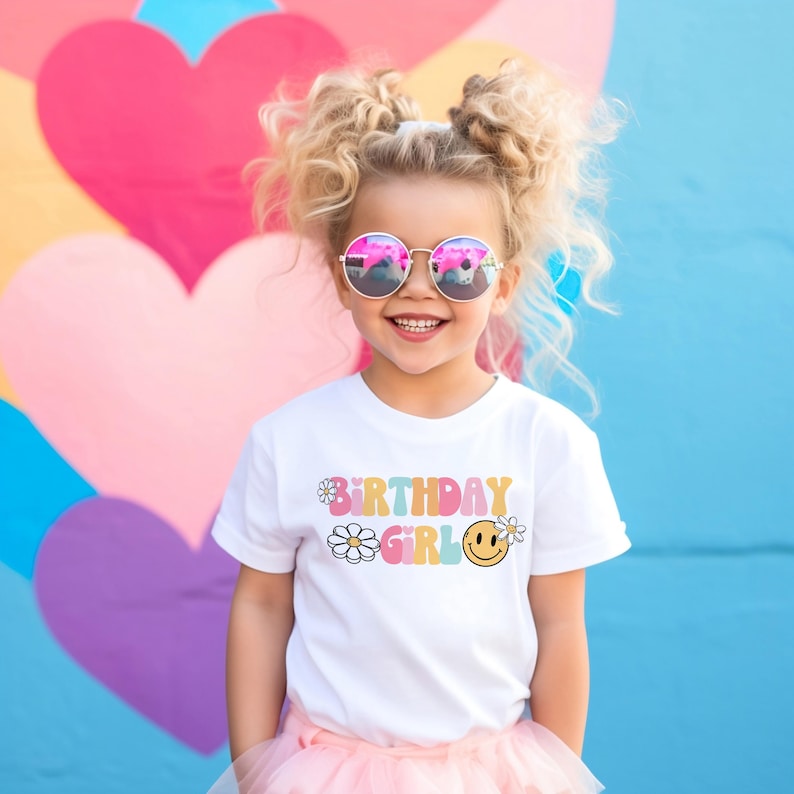 May include: A white t-shirt with a colorful "Birthday Girl" graphic featuring daisies and a smiley face. The shirt is worn by a young girl with blonde hair and pink sunglasses.