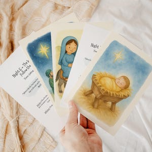 Może przedstawiać: Ręka trzyma stos ilustrowanych kart o tematyce religijnej. Karty przedstawiają akwarelowe obrazy scen biblijnych, w tym gwiazdę, kobietę na osiołku i dziecko w żłobie. Tekst na kartach brzmi "Night 6 - The V Follow the star".
