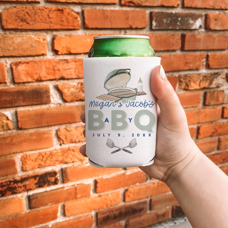 May include: White can cooler with a BBQ theme. The design includes a grill illustration, the text "Megan's Jacob's BABY BBQ" and the date July 9, 20XX. The cooler also features crossed spatulas.