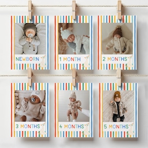 May include: A set of six baby milestone photo cards, each featuring a different month or newborn. The cards are decorated with colorful vertical stripes and wooden clothespins. Each card has a photo of a baby.