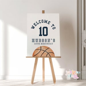 May include: White sign with blue text that says "Welcome to 10 Hudson's 10th Birthday". A brown basketball with black lines is at the bottom of the sign.