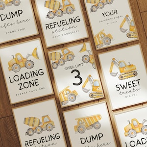 May include: A collection of framed signs with watercolor illustrations of construction vehicles. The signs feature text such as "DUMP gifts here," "REFUELING station," "LOADING ZONE," and "SWEET treats." The signs are in a neutral color palette.