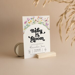May include: A baby shower invitation with a floral design and the text "Baby in Bloom" in a retro font. The invitation includes the name Alexandra Jones, the date October 18th, and the time 12 PM. The location is The Clare Home, 100 Juniper Rd, Boulder, CO 80125.