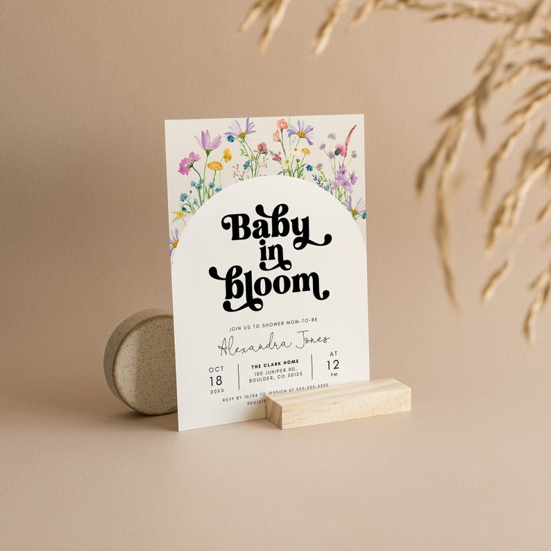 May include: A baby shower invitation with a floral design and the text "Baby in Bloom" in a retro font. The invitation includes the name Alexandra Jones, the date October 18th, and the time 12 PM. The location is The Clare Home, 100 Juniper Rd, Boulder, CO 80125.