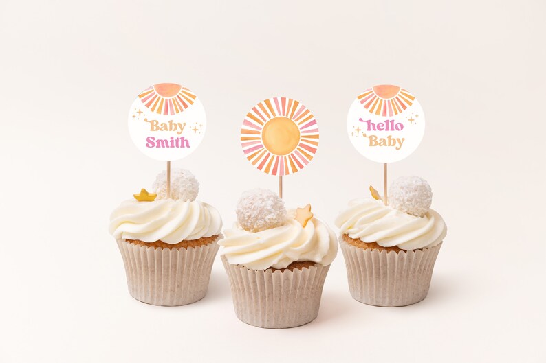 Peut inclure: Trois cupcakes d&eacute;cor&eacute;s de gla&ccedil;age blanc et surmont&eacute;s d'une &eacute;toile dor&eacute;e et d'un rond de papier blanc. Les d&eacute;corations pr&eacute;sentent un soleil aquarelle avec des rayures roses et orange et un texte qui dit "Baby Smith", "Hello Baby" et un soleil avec des rayures roses et orange.