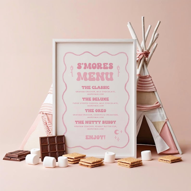 May include: A framed pink and white "S'Mores Menu" sign with a teepee in the background. The menu lists s'mores variations: The Classic, The Deluxe, The Oreo, and The Nutty Buddy. Marshmallows, graham crackers, and chocolate bars are arranged in front.