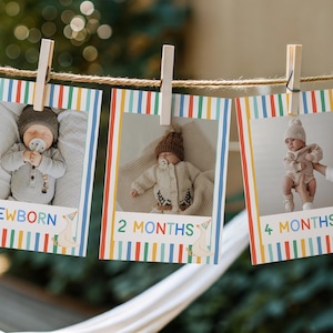 Puede incluir: Tres tarjetas de hitos rectangulares colgadas de una cuerda con pinzas de madera. Cada tarjeta presenta un borde de rayas verticales de colores, una fotograf&iacute;a de beb&eacute; y el texto NEWBORN, 2 MONTHS y 4 MONTHS con un peque&ntilde;o gr&aacute;fico de gorro.