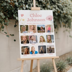 Puede incluir: Un letrero rosa claro sobre un caballete de madera con el nombre "Chloe Johnson" y "Boulder High Class of 20XX." El letrero muestra doce fotos peque&ntilde;as de ni&ntilde;as, cada una etiquetada con un n&uacute;mero de grado del 1&ordm; al 12&ordm;.