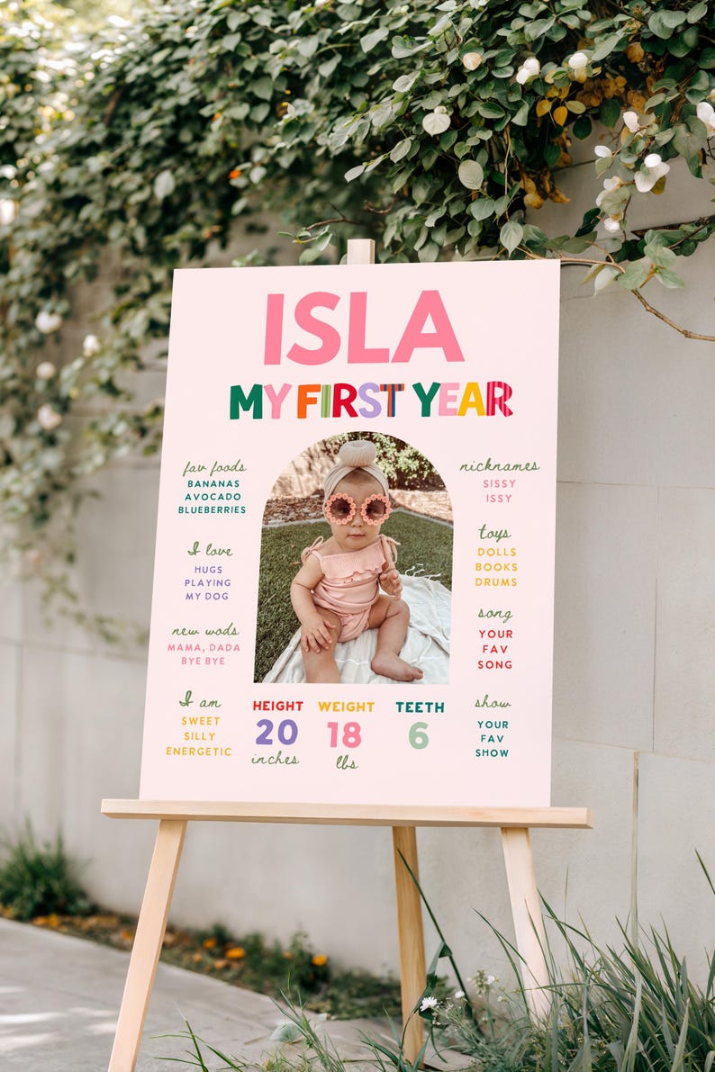 May include: A pink milestone birthday sign titled ISLA MY FIRST YEAR featuring a central photo of a baby wearing flower sunglasses. The board lists facts including fav foods, nicknames, toys, and stats of 20 inches, 18 lbs, and 6 teeth.