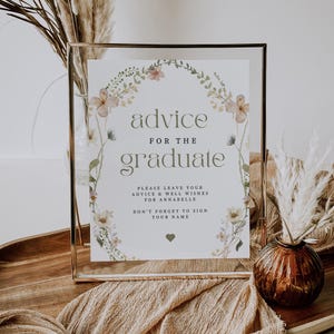 Pu&ograve; includere: Un cartello incorniciato con la scritta "advice for the graduate" in un elegante carattere, circondato da una ghirlanda floreale. Il cartello include una richiesta di consigli e auguri per Annabelle, con l'invito a firmare.