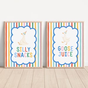 May include: Two framed prints with a colorful vertical striped background. Each print features a white goose wearing a party hat inside a blue cloud shape. One print says "SILLY SNACKS" and the other says "GOOSE JUICE".