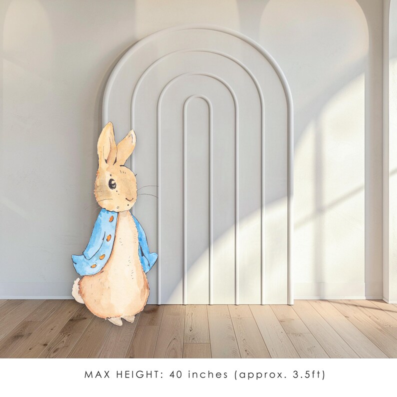May include: A blue and brown Peter Rabbit cutout, standing in front of a white wall with an arched doorway. The cutout is 40 inches tall.