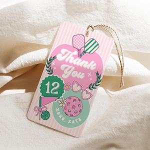May include: Pink and white striped gift tag with a pickleball theme. The tag features the words "Thank You" in a retro font, along with pickleball paddles, a pickleball, and the number 12. A twine string is attached.