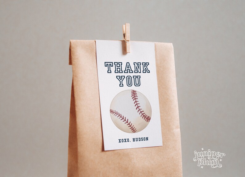 Peut inclure: Une carte de remerciement blanche avec du texte noir qui dit "THANK YOU" et un graphique de baseball. La carte est attach&eacute;e &agrave; un sac en papier brun avec une pince &agrave; linge en bois. Le texte au bas de la carte dit "XOXO. HUDSON".