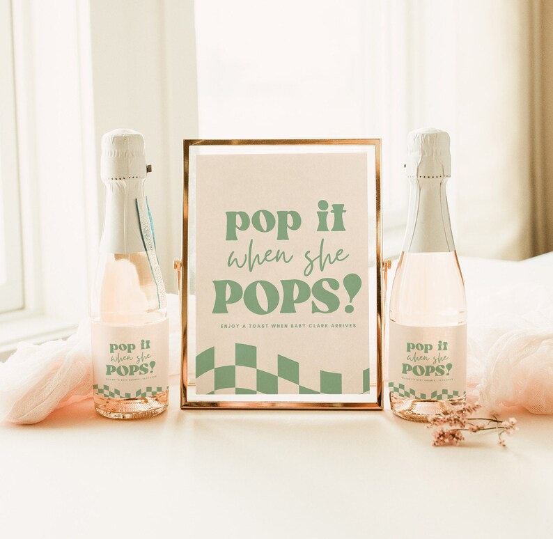 May include: Two glass bottles with custom labels featuring sage green text that reads pop it when she POPS! and a checkered pattern. Between the bottles stands a gold-framed sign with the same text and a sage green checkered base design.