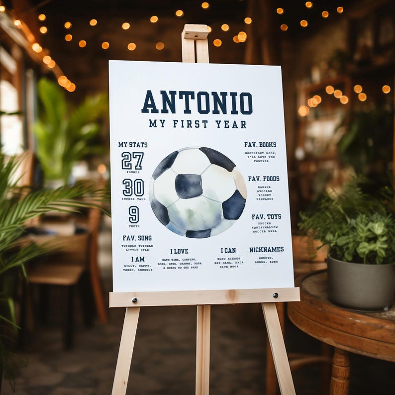 May include: A white poster board with a blue and white watercolor soccer ball illustration. The poster board has the text "Antonio My First Year" at the top and lists various stats, favorite songs, foods, books, toys, and nicknames.