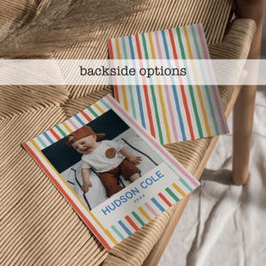 Puede incluir: Dos tarjetas rectangulares con un borde de rayas verticales de colores rojo, naranja, amarillo, verde y azul. Una tarjeta muestra la fotograf&iacute;a de un ni&ntilde;o con gorra marr&oacute;n y camiseta blanca, con el texto HUDSON COLE 20XX impreso debajo.