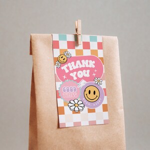 May include: A pink and orange thank you tag with a checkered background. The tag features a pink circle with the text "Thank You" in white. There are also smiley faces, flowers, and the text "Good Times" in a purple circle.