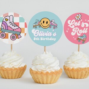 May include: Three cupcake toppers with a roller skate theme. The toppers feature a pink roller skate with rainbow accents, a blue roller skate with a smiley face, and a pink roller skate with the text "Let's Roll".