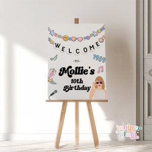 May include: Welcome to Mollie's 10th Birthday party sign with a colorful banner, a microphone, a cowboy boot, a music note, and a cartoon image of Taylor Swift. The sign is on an easel.