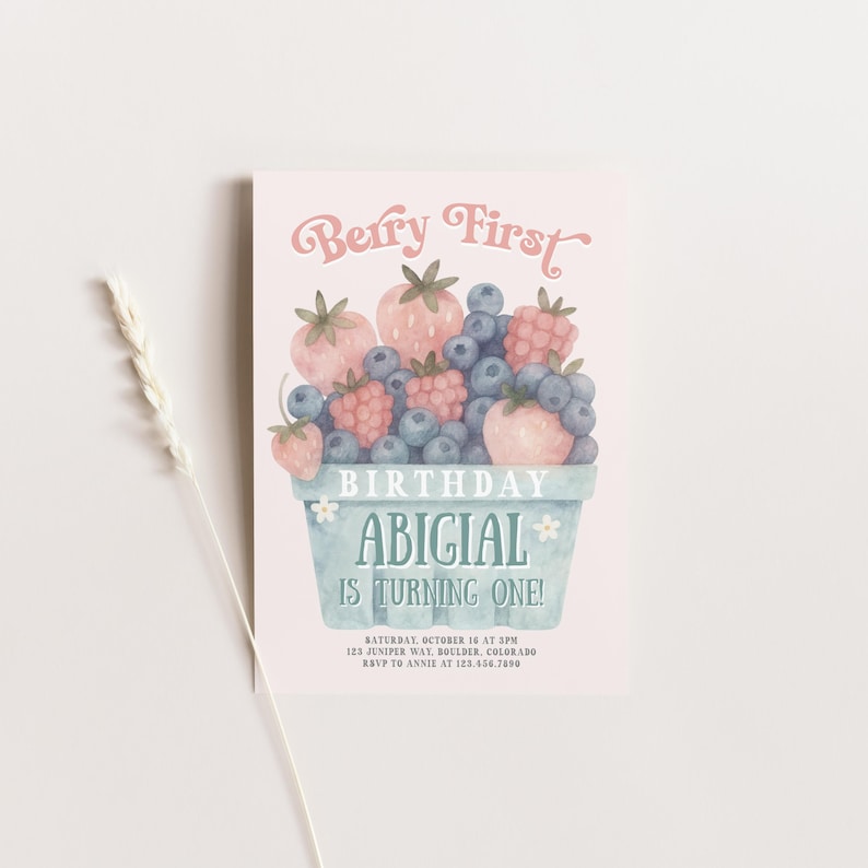 May include: A light pink birthday invitation with watercolor illustrations of strawberries and blueberries in a blue basket. The text "Berry First" and "Abigail is turning one!" are displayed in a whimsical font.