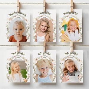 May include: A series of school year photo cards, each featuring a child's portrait within a floral wreath. The cards are labeled with grade levels from Kindergarten to 5th grade and corresponding years, clipped to a string with wooden clothespins.