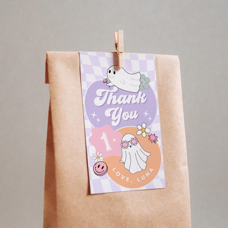 May include: A brown paper bag with a decorative tag. The tag features a purple and orange design with the words "Thank You" and "Love, Luna". It includes illustrations of ghosts, flowers, and a smiley face.