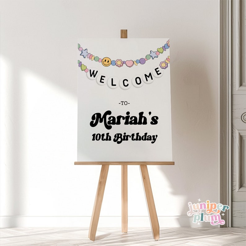 May include: White welcome sign with a colorful beaded garland and the text "Welcome to Mariah's 10th Birthday".