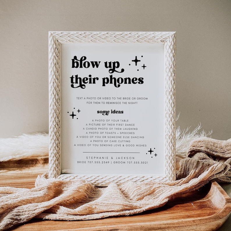 K&ouml;nnte beinhalten: Ein wei&szlig; gerahmtes Schild mit schwarzem Text, der "blow up++ their phones" lautet. Das Schild fordert die G&auml;ste auf, ein Foto oder Video an die Braut und den Br&auml;utigam zu schicken, mit einigen Ideen, was sie schicken k&ouml;nnen, wie zum Beispiel ein Foto ihres ersten Tanzes oder ein Video vom Anschneiden der Torte. Das Schild enth&auml;lt auch die Namen und Telefonnummern der Braut und des Br&auml;utigams.