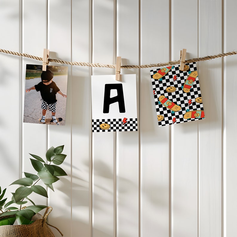 May include: Three white photo cards with black borders are hanging on a string with wooden clothespins. The cards feature a black and white checkered pattern with a smiley face and skateboard graphic. The center card has a large black letter "A" on a white background. The card on the left shows a photo of a young child wearing a black shirt and shorts, standing on a skateboard.
