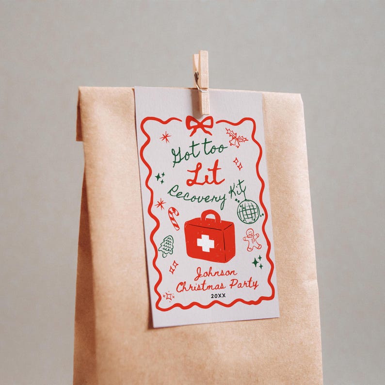 Puede incluir: Una tarjeta blanca con una ilustraci&oacute;n roja y verde de un botiqu&iacute;n de primeros auxilios con el texto "Got too Lit Recovery Kit" y "Johnson Christmas Party 20XX" adjunta a una bolsa de papel marr&oacute;n con una pinza de madera.
