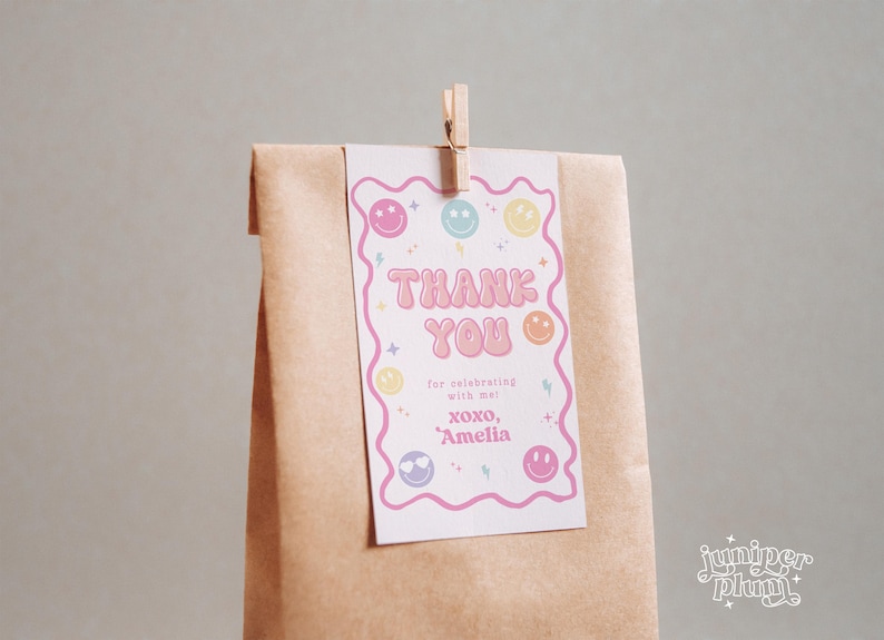 Pu&ograve; includere: Un biglietto di ringraziamento rosa e bianco con un bordo ondulato e faccine sorridenti colorate. Il testo sul biglietto dice "Grazie per aver festeggiato con me! xoxo, Amelia".