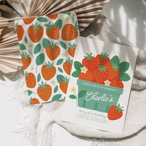 May include: A white card and matching fabric with a strawberry theme. The card reads "Charlie's berry first birthday" with a basket of strawberries. The fabric has a repeating pattern of strawberries and leaves.