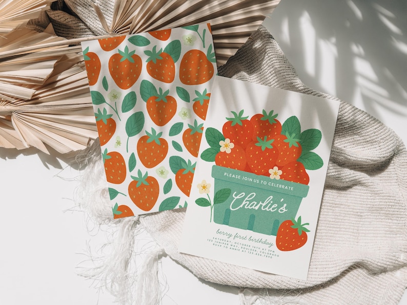 May include: A white card and matching fabric with a strawberry theme. The card reads "Charlie's berry first birthday" with a basket of strawberries. The fabric has a repeating pattern of strawberries and leaves.