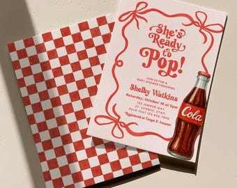 Puede incluir: Una invitación para un baby shower con el texto "She's Ready to Pop!" en escritura roja. La invitación presenta un borde rojo con lazos y una ilustración de acuarela de una botella de cola. Se ve un patrón a cuadros rojo y blanco a juego.