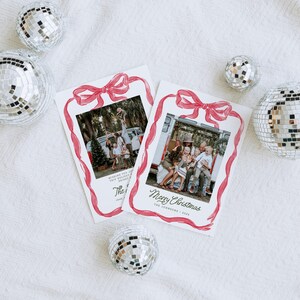 May include: Two Christmas cards featuring family photographs, framed with a red watercolour bow and ribbon design. Silver disco balls are scattered around the cards on a white textured surface. One card says "Merry Christmas".