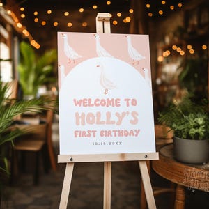 K&ouml;nnte beinhalten: Ein rosa-wei&szlig;es Willkommens-Schild mit einem Cartoon-G&auml;nse-Design. Das Schild lautet "Willkommen zu Hollys erstem Geburtstag 10.15.20XX".