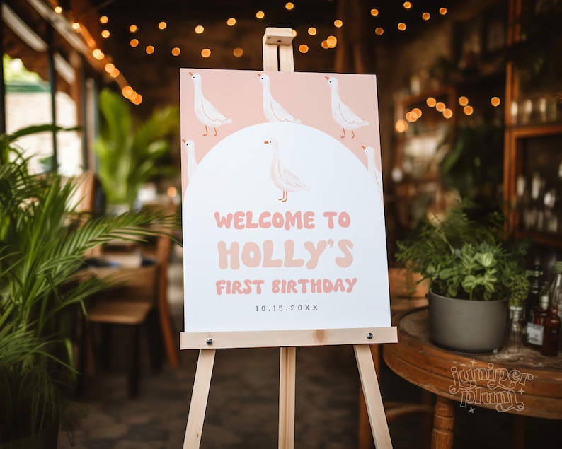 K&ouml;nnte beinhalten: Ein rosa-wei&szlig;es Willkommens-Schild mit einem Cartoon-G&auml;nse-Design. Das Schild lautet "Willkommen zu Hollys erstem Geburtstag 10.15.20XX".