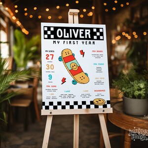 May include: A white poster with black and white checkered borders, featuring a colorful skateboard graphic and text that reads "Oliver My First Year". The poster includes details about Oliver's first year, such as his favorite songs, books, foods, and toys.