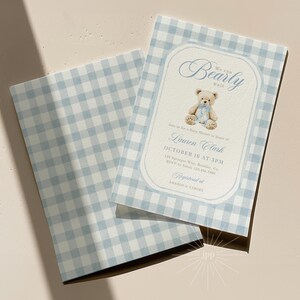 May include: Baby shower invitation with a light blue and white gingham pattern. The invitation features a teddy bear illustration and the text "We can bearly wait". The invitation is for Lauren Clark, October 16 at 3PM.