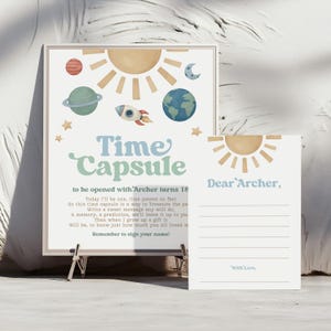 May include: A framed print and matching card set. The print features a celestial theme with a sun, planets, and a rocket ship in pastel colours. Text on the print reads "Time Capsule" and "Dear Archer."